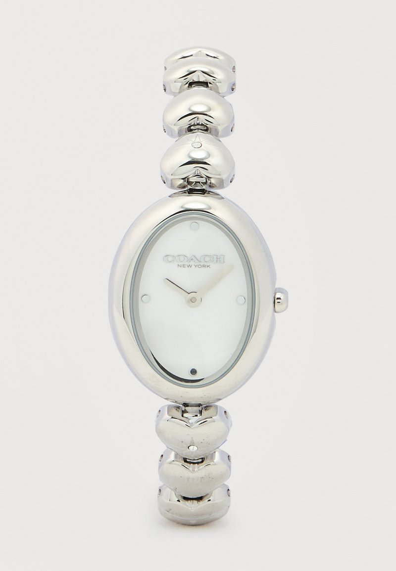 Ασημένιο ρολόι χειρός Coach με οβάλ λευκό καντράν και αλυσίδα σε σχήμα καρδιάς, δείχνει ώρα 11:07.