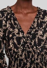 Black floral dress featuring a ruffled neckline, long sleeves, and a smocked waist with beige floral patterns throughout.