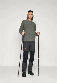 Gray, textured sweater with a round neckline, paired with dark cargo pants featuring pockets and reinforced patches, held with trekking poles.