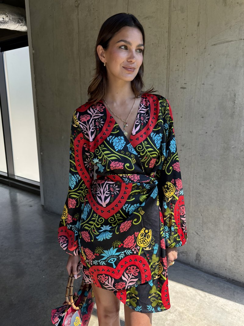Μαύρο φόρεμα περιτύλιξης με πολύχρωμα λουλουδάτα σχέδια σε κόκκινο, μπλε και πράσινο. Μακριά μανίκια, ντεκολτέ σε σχήμα V και λεπτομέρεια με κορδόνι στη μέση.
