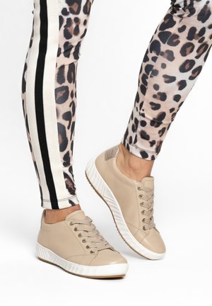Legs wearing leopard-print leggings with black and white side stripes paired with beige casual lace-up sneakers with white soles.