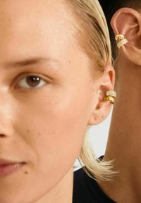 Close-up van twee oren met gouden en met diamanten bezette oorclips, één met blond haar en de ander met een donkere huid en kort haar.