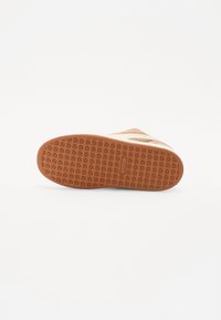 Brown rubber sneaker sole featuring a textured pattern, with beige accents along the side and a smooth finish.