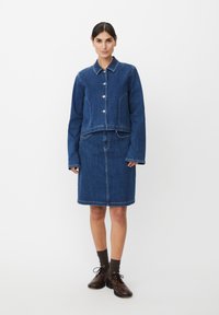 Veste en denim avec boutons à l'avant et deux poches, assortie à une jupe en denim de la même couleur. Les deux sont d'un bleu profond avec des surpiqûres contrastantes.