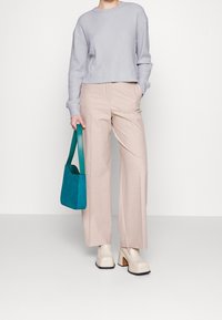 Lichtpaarse cropped sweater, beige wijde broek, witte platform schoenen en een teal suède handtas met een groene schouderband.