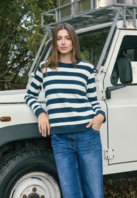 Sweat-shirt à rayures bleu marine et blanches avec un col rond, des poignets et un ourlet côtelés. Porté avec un jean bleu, debout à côté d'un véhicule blanc.