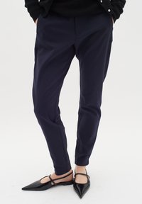 Námořnické zúžené kalhoty s hladkým materiálem, se bočními kapsami a elegantním siluetu, spárované s černými páskovými špičatými byty.