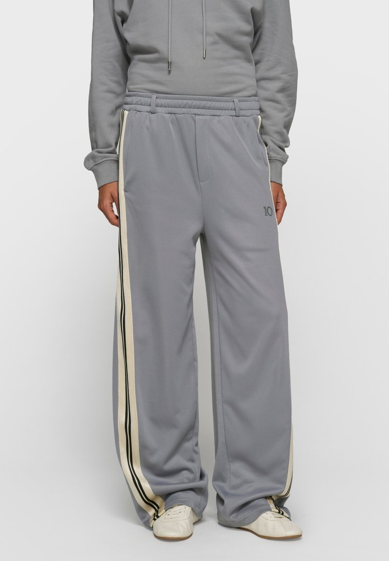 Pantalon de survêtement gris à jambes larges avec des rayures ivoire et noires sur les côtés, taille élastique et poches latérales. Texture douce, coupe décontractée.