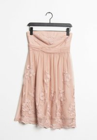 Utan axelband, rosa klänning med blommönster, utsvängd kjol och spetsdetaljer vid fållen. Tillverkad i lätt material, hänger på en svart krok.