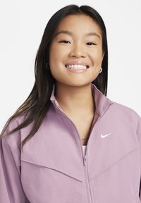 Světle fialová zipová bunda s vysokým límcem, vyrobená z hladkého materiálu, s bílým logem Nike na hrudi a jemnými designovými detaily.