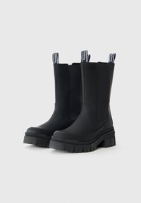 Bottines noires en caoutchouc lisse, avec des panneaux latéraux élastiques et une semelle épaisse texturée. Dotées de languettes de marque pour un enfilage facile.