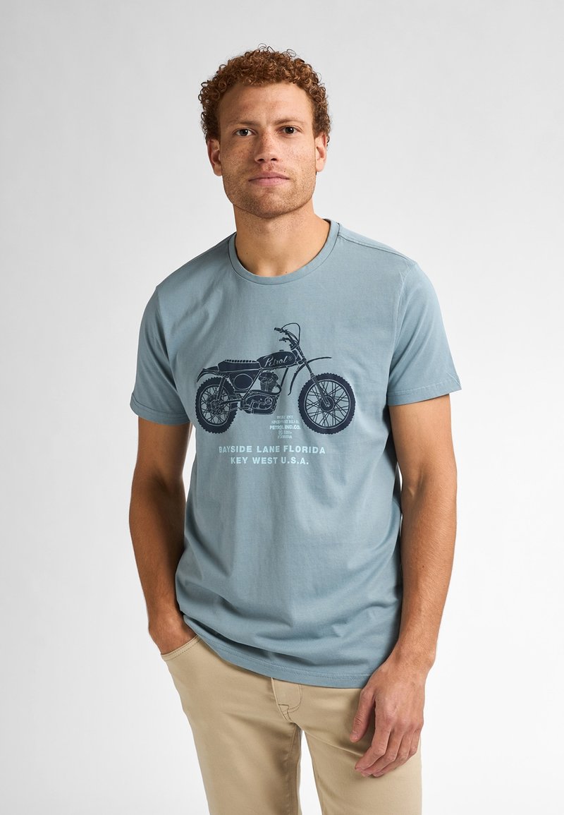 Světle modré bavlněné tričko se vzorem tmavého motocyklu a textem: "Bayside Lane Florida Key West U.S.A."