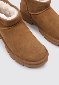 Braune Wildleder-Stiefeletten mit weichem Innenfutter, runder Zehenpartie und dicker Gummisohle. Sichtbare Nähte und ein umgeschlagener Schaft.