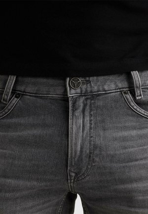 Nærbillede af grå denimjeans med sort top stoppet ned, der viser forreste knap, lynlås, bæltestropper og lommer.