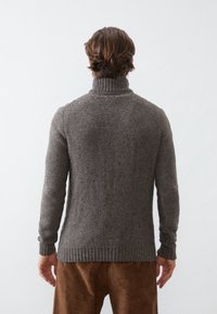 Maglione grigio lavorato a maglia con collo alto, motivo a trama, polsini e orlo a coste. Indossato sopra pantaloni marroni di velluto a coste.