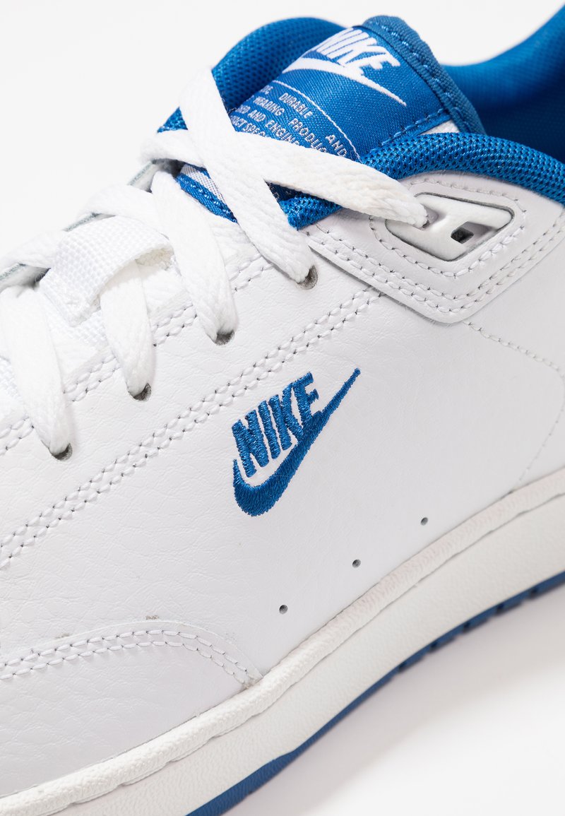 Białe skórzane sneakersy z niebieskimi akcentami, z teksturowaną powierzchnią, płaskimi białymi sznurowadłami oraz niebieską siateczkową językiem z detalem z logo.