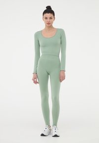 Top a maniche lunghe verde chiaro e leggings in una texture a coste, abbinati a scarpe sportive bianche e nere. Design aderente su tutta la lunghezza.