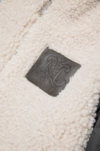 Lichtbeige fleece-stof met een getextureerde afwerking, voorzien van een donker leren patch met een intrigerend ontwerp en een ritssluiting.