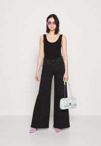 Sort bodysuit med scallop-kant, parret med brede sorte jeans. Accessories inkluderer en pastelfarvet geometrisk taske og lavendel solbriller.