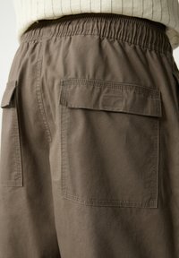 Bruine katoenen cargobroek met een elastische tailleband, voorzien van twee achterzakken en opvallende stikseldetails. Gestructureerde stof met een ontspannen pasvorm.