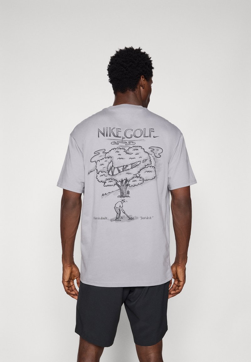 Siva bomba majica iz bombaža s grafičnim dizajnom koji prikazuje drvo i golf igrača. Natpisi "NIKE GOLF" i "Kada sumnjaš... 'Samo uradi to.'" u crnoj boji.