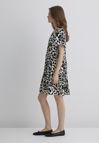 Kurzärmeliges Kleid in einem cremefarbenen und schwarzen abstrakten Muster, mit einem gestuften Design und einer lockeren Passform. Kombiniert mit schwarzen Ballerinas.