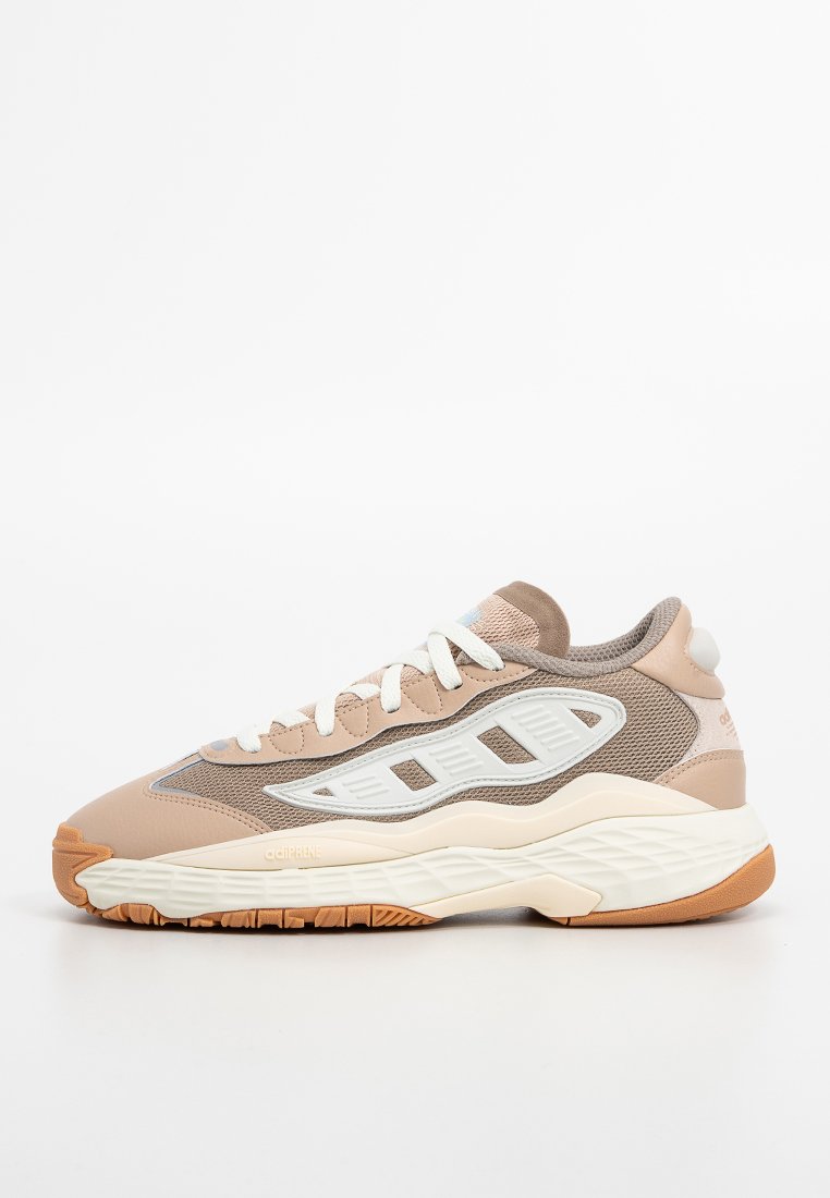 Scarpa sportiva in tonalità beige, con parte superiore in mesh e sovrapposizioni sintetiche, dettagli bianchi, chiusura con lacci e suola in gomma testurizzata.