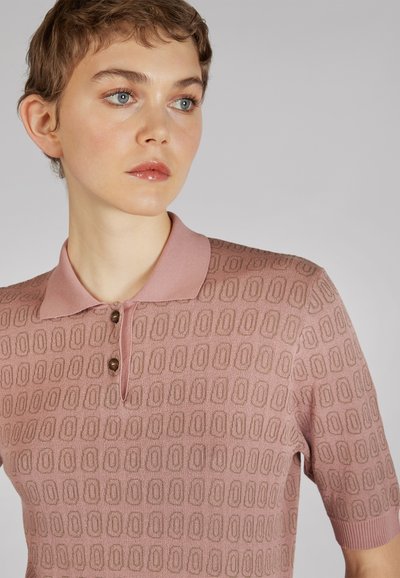 Sweter polo w jasnoróżowym kolorze, z krótkimi rękawami, z tłoczonym geometrycznym wzorem oraz dwoma guzikami w kolorze brązowym.