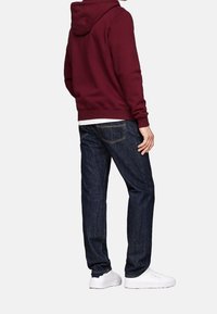 Burgundy hoodie med en känguruficka, matchad med mörkblå denimjeans som har en femficksdesign och vita sneakers.