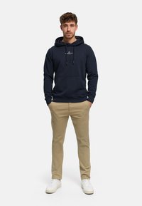 Laivastonsininen huppari, jossa etutasku ja kiristysnauhat, yhdistetty vaaleanbeigeihin housuihin ja valkoisiin tennareihin. Yksinkertainen malli ilman kuvioita.