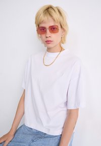 Biele oversized tričko s okrúhlym výstrihom a krátkymi rukávmi, doplnené o tónované obrdlhé slnečné okuliare a zlatý náhrdelník.