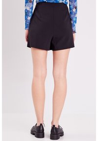 Shorts noirs avec une coupe ajustée, une taille élastique et une texture lisse. Associés à des chaussures noires et à un haut à motifs visible.