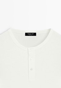 Hvid langærmet Henley-shirt med tre knapper og en sort Massimo Dutti-label ved halsudskæringen.