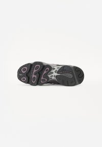 Black athletic shoe outsole with purple accents, featuring a textured rubber surface, patterned tread, and visible branding on the heel.