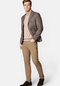 Marynarka w kratę w odcieniach brązu i niebieskiego, beżowy golf, khaki spodnie, ciemne buty oraz podwinięte rękawy, tworząc nowoczesny, dopasowany styl.