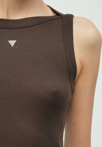 Rjava top brez rokavov iz mehkega blaga, z diamantno oblikovanim kristalnim poudarkom na izrezu. Gladek tekstura, oprijet kroj.