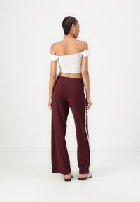Top court blanc à épaules dénudées associé à un pantalon large taille haute bordeaux avec une rayure verticale contrastante. Texture lisse.