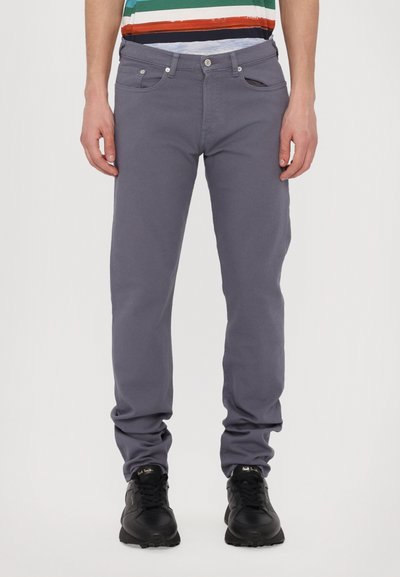 Jeans en coton gris avec une coupe slim, design cinq poches, boutons en métal et léger élasthanne ; associés à des chaussures de sport noires.