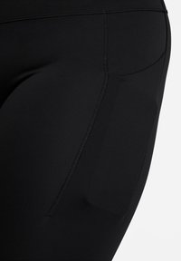 Sorte treningsleggings med en glatt tekstur, tettsittende design og en sidelomme. Sømmene er synlige langs kantene.