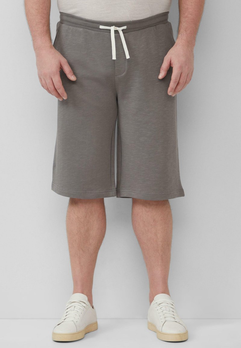 Grau Shorts aus weichem, dehnbarem Stoff mit einem Kordelzugbund, seitlichen Taschen und einer lockeren Passform, kombiniert mit weißen Turnschuhen.