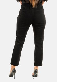 Pantaloni in corduroy neri con un design aderente, dotati di tasche posteriori e gamba svasata. Indossati con scarpe con tacco alto nere.