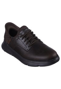 Zapatilla de cuero marrón con un talón texturizado en color canela, puntera redonda y suela de goma negra. Presenta cordones marrones medios y un logotipo en el lateral.
