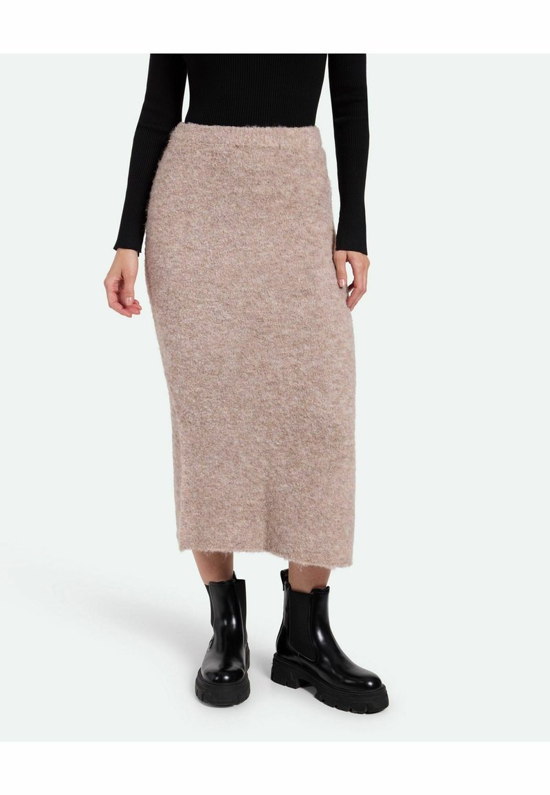 Helles Beige, gestrickter Midikilt mit strukturiertem Finish und fransigem Saum, kombiniert mit schwarzen, klobigen Knöchelstiefeln.