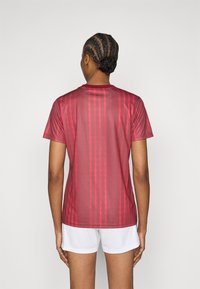 Κόκκινο αθλητικό μπλουζάκι με στρογγυλή λαιμόκοψη, που διαθέτει ζιγκ-ζαγκ μοτίβο σε ελαφρώς πιο σκούρο τόνο, κατασκευασμένο από λείο, ελαφρύ ύφασμα.