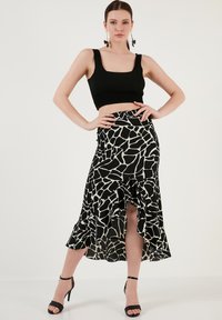 Un top scurt fără mâneci de culoare neagră, asortat cu o fustă cu model negru și bej, având un tiv evazat și o fanta laterală. Sandale cu toc înalt, de culoare neagră.