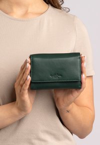 Groene leren portemonnee met een klepsluiting, met een gladde textuur en embossed branding. Compact rechthoekig van vorm, makkelijk in de hand te houden.