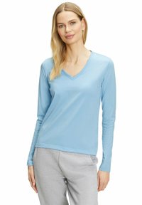 Hellblaues langärmliges V-Ausschnitt-Oberteil aus glattem Stoff, kombiniert mit grauen Jogginghosen. Das Shirt hat einen lässigen Schnitt und ein minimalistisches Design.