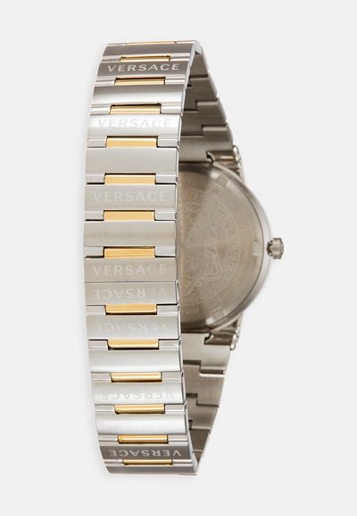 Hõbedane ja kuldne metallist käekell, millel on graveeritud "VERSACE" tekst linkide kohal, ümmargune korpus ja sile tekstuuriga tagumine külg.