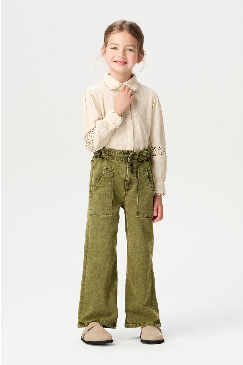 Helle beige Bluse mit einem Spitzenkragen, kombiniert mit hochtaillierten, olivgrünen, weit geschnittenen Hose mit großen Fronttaschen.