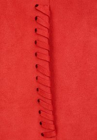 Gros plan sur un tissu en daim rouge avec une couture décorative en point de surjet qui court verticalement au centre.
